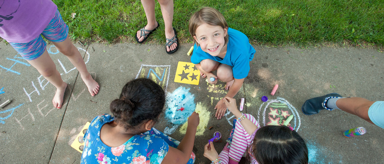 Children coloring a sidewalk with colored chalk during the IYWP Outdoor Poetry Camp 2018.