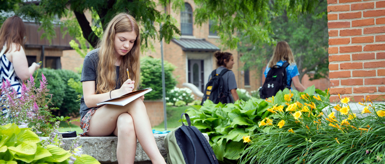 A female student writing on a bench outdoors.